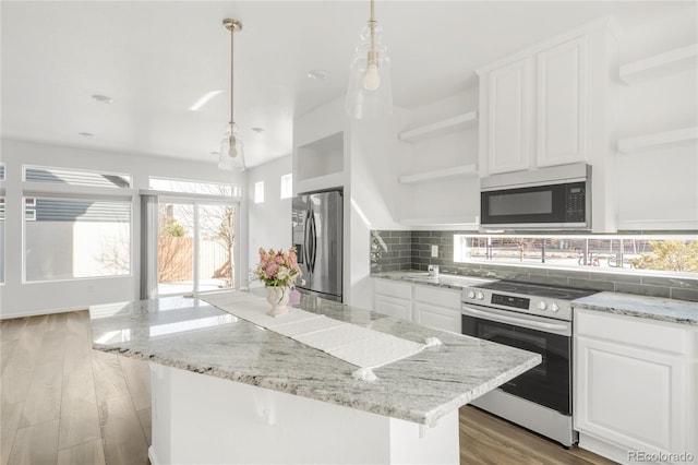 kitchen with light wood-style flooring, open shelves, tasteful backsplash, a center island, and stainless steel appliances