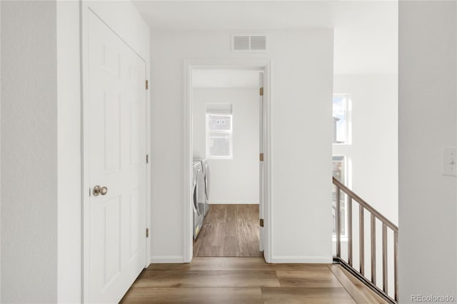 corridor featuring wood finished floors, baseboards, visible vents, an upstairs landing, and washer and clothes dryer