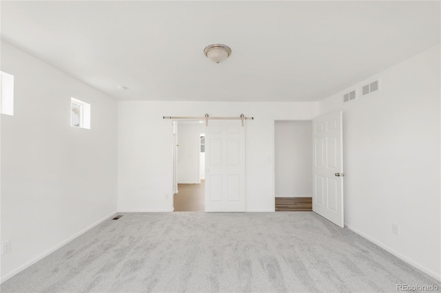 spare room with a barn door, visible vents, baseboards, and carpet