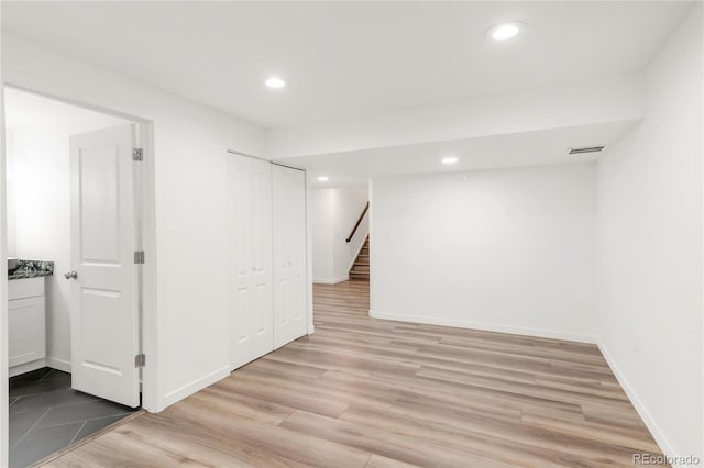 finished basement with light wood finished floors, visible vents, baseboards, stairs, and recessed lighting