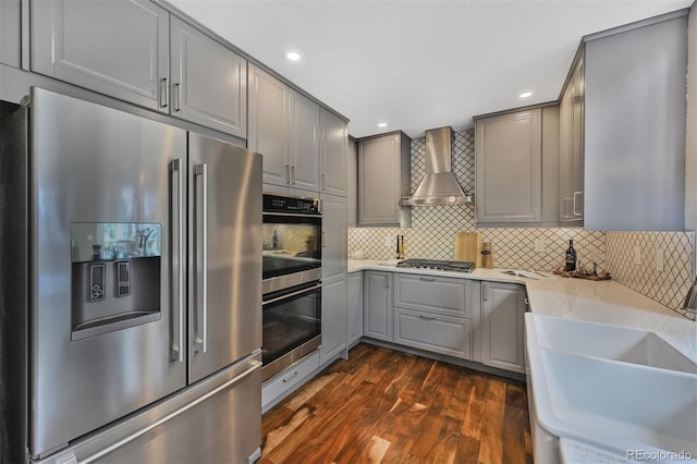 kitchen with gray cabinets, dark wood-style floors, stainless steel appliances, wall chimney exhaust hood, and a sink