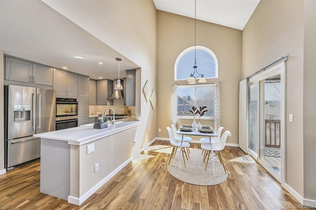 kitchen with wall chimney exhaust hood, gray cabinetry, wood finished floors, and stainless steel appliances