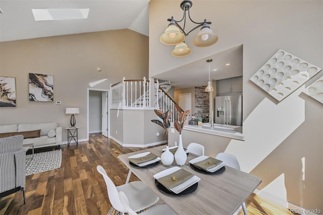 dining room featuring a notable chandelier, wood finished floors, a skylight, baseboards, and stairs