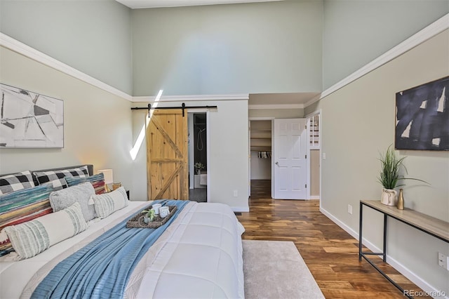 bedroom featuring a barn door, wood finished floors, baseboards, and a towering ceiling