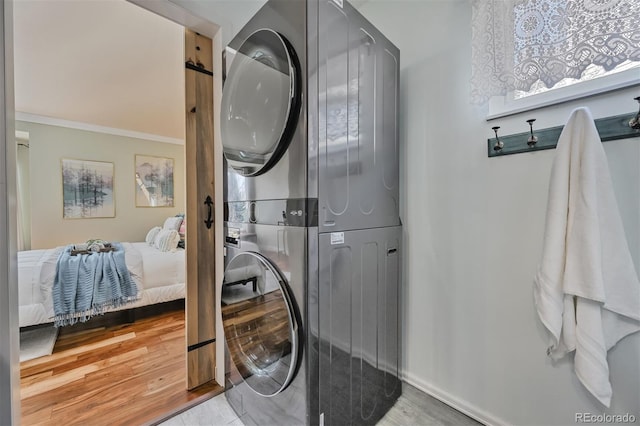 clothes washing area featuring wood finished floors, baseboards, laundry area, stacked washer and clothes dryer, and crown molding