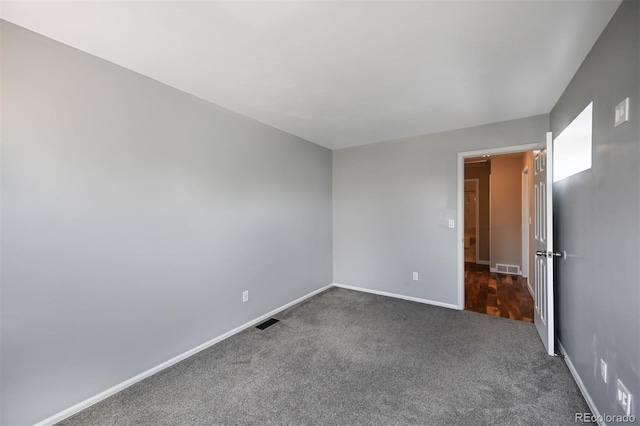 unfurnished room featuring visible vents, dark carpet, and baseboards