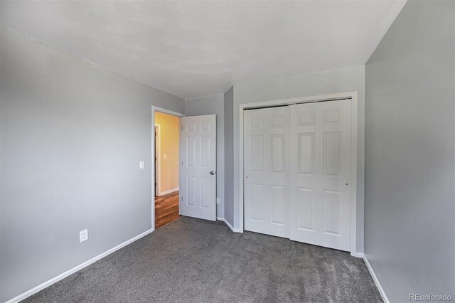 unfurnished bedroom featuring baseboards, dark colored carpet, and a closet