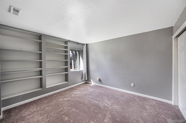 carpeted spare room with visible vents, built in features, a textured ceiling, baseboards, and a textured wall