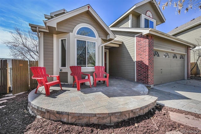 view of front facade with a garage, brick siding, driveway, and fence