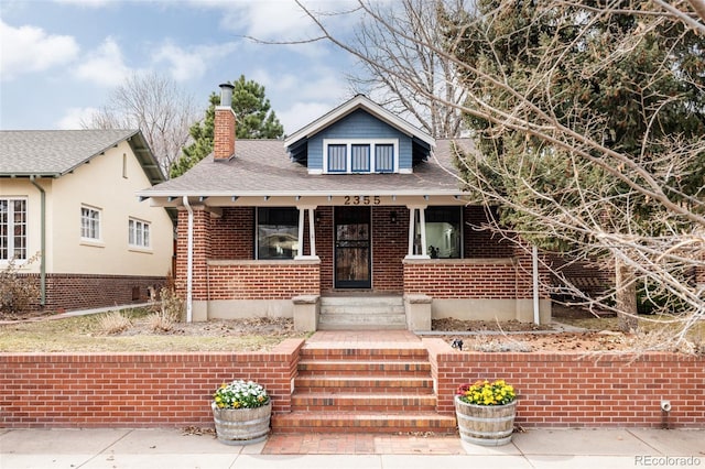 bungalow featuring roof with shingles, a chimney, and brick siding