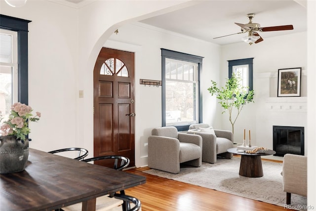 foyer entrance with arched walkways, ornamental molding, a glass covered fireplace, ceiling fan, and wood finished floors