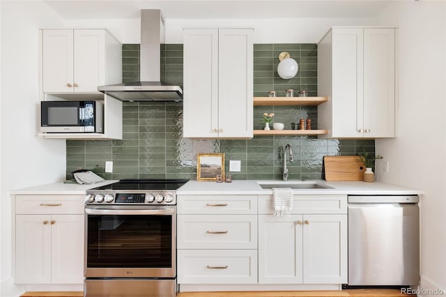 kitchen featuring appliances with stainless steel finishes, light countertops, wall chimney range hood, white cabinetry, and a sink