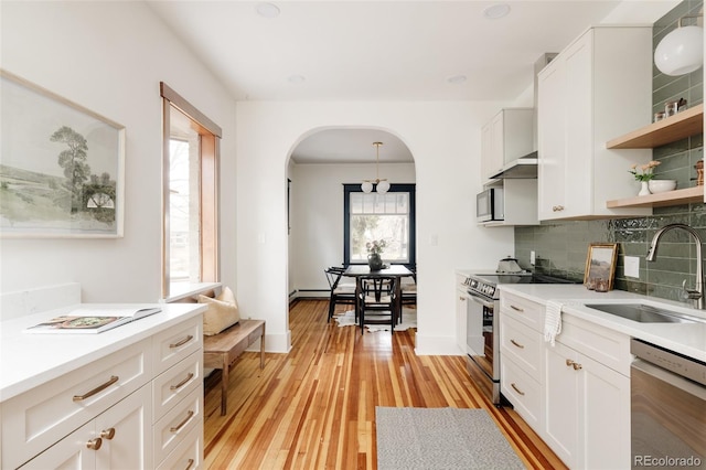 kitchen featuring open shelves, light wood-style flooring, decorative backsplash, appliances with stainless steel finishes, and a sink