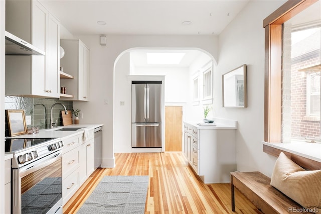 kitchen featuring light wood-style flooring, a sink, stainless steel appliances, open shelves, and backsplash