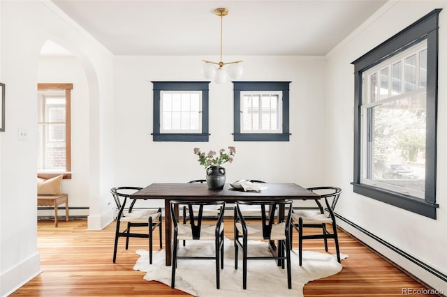 dining space featuring arched walkways, baseboards, a baseboard radiator, light wood-style floors, and a baseboard heating unit