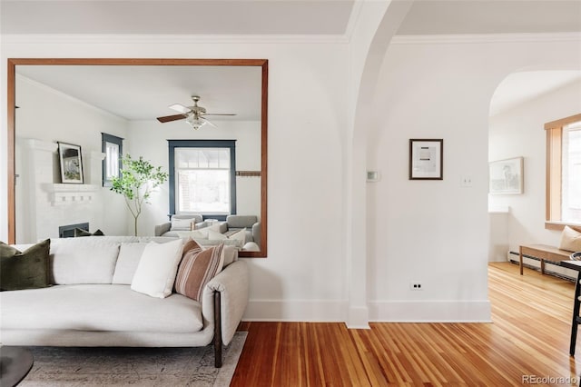 living area featuring arched walkways, baseboards, wood finished floors, and crown molding