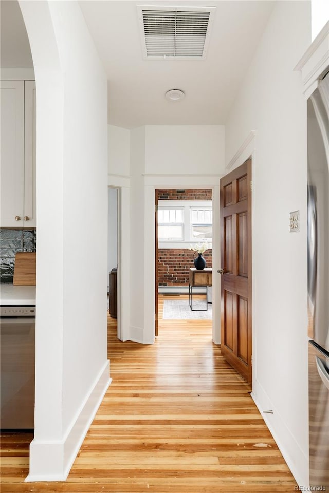 corridor with arched walkways, baseboards, visible vents, and light wood-style floors