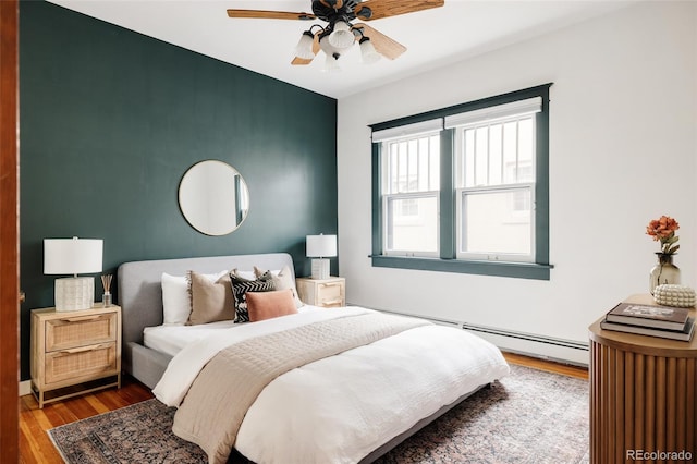 bedroom featuring ceiling fan, an accent wall, a baseboard heating unit, and wood finished floors