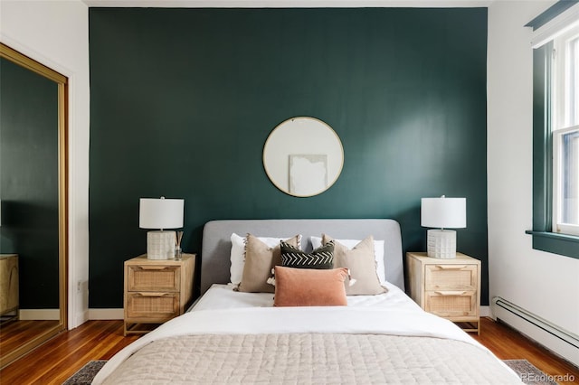 bedroom with a baseboard heating unit, an accent wall, wood finished floors, and baseboards