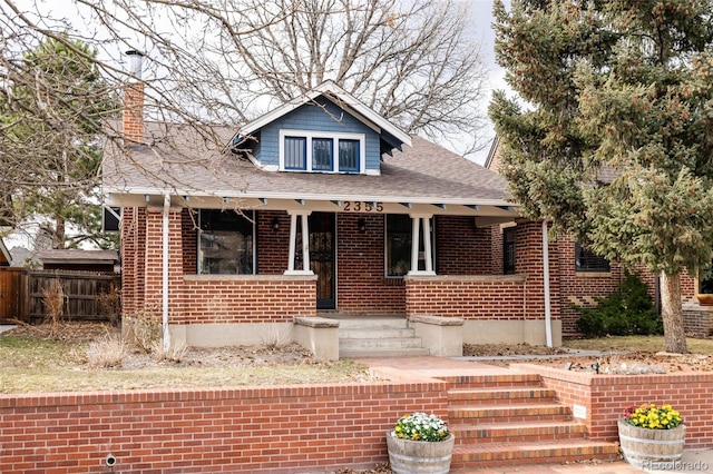 bungalow-style house featuring a porch, brick siding, fence, and roof with shingles