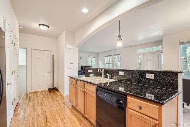 kitchen with hanging light fixtures, sink, dark stone countertops, black dishwasher, and light wood-type flooring