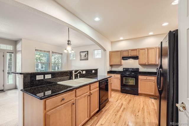 kitchen featuring pendant lighting, light wood-type flooring, sink, black appliances, and a center island with sink