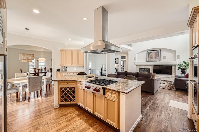 kitchen featuring island exhaust hood, light wood-type flooring, tasteful backsplash, a glass covered fireplace, and stainless steel gas stovetop