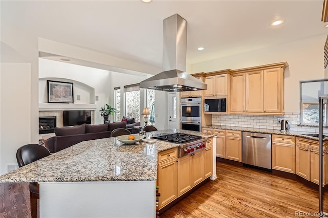 kitchen featuring tasteful backsplash, a kitchen island, island exhaust hood, stainless steel appliances, and a fireplace