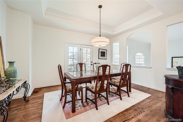 dining area featuring plenty of natural light, a tray ceiling, arched walkways, and dark wood finished floors