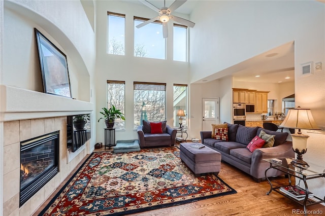 living room with ceiling fan, a tiled fireplace, visible vents, and light wood-style floors