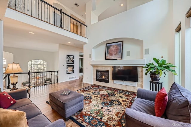 living area featuring a tile fireplace, visible vents, a high ceiling, and wood finished floors