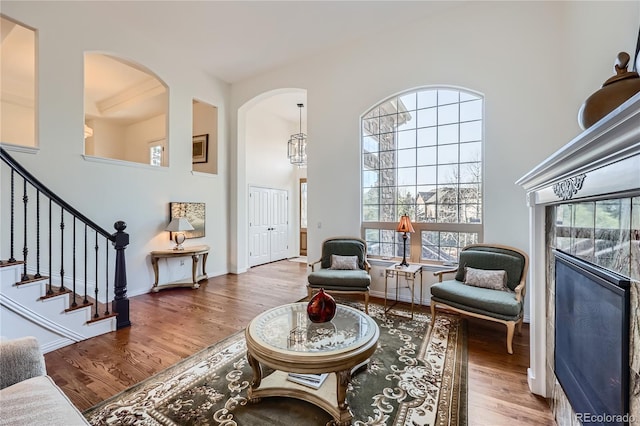 sitting room featuring a towering ceiling, a tiled fireplace, wood finished floors, baseboards, and stairs