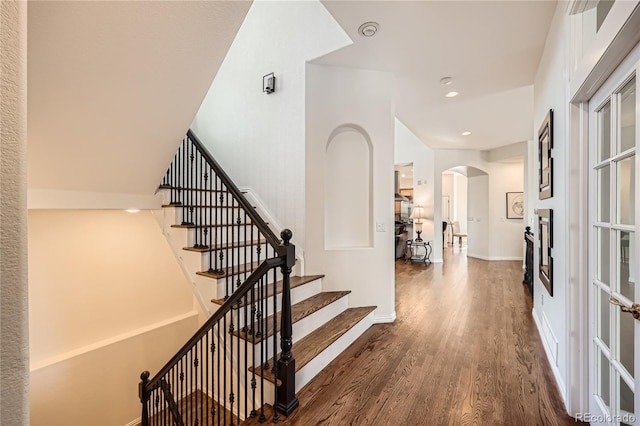 stairs featuring baseboards, arched walkways, and wood finished floors