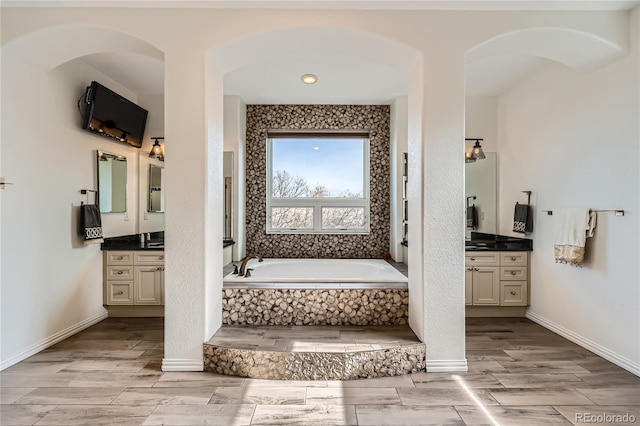 full bath featuring baseboards, wood finish floors, a bath, and vanity