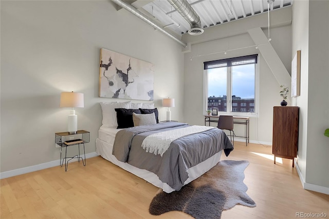 bedroom with a towering ceiling and hardwood / wood-style floors