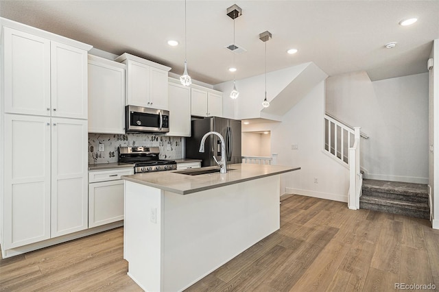 kitchen with white cabinets, an island with sink, hanging light fixtures, appliances with stainless steel finishes, and light hardwood / wood-style floors