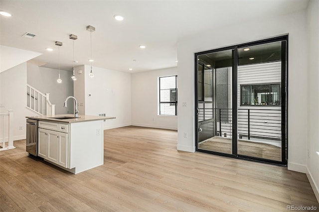 kitchen featuring sink, white cabinetry, light hardwood / wood-style flooring, a center island with sink, and decorative light fixtures