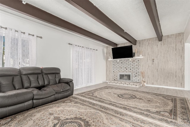 living area featuring wooden walls, beamed ceiling, a fireplace, wood finished floors, and a textured ceiling