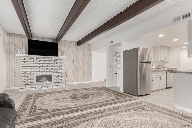 living area featuring light wood-type flooring, visible vents, beam ceiling, a textured ceiling, and a fireplace