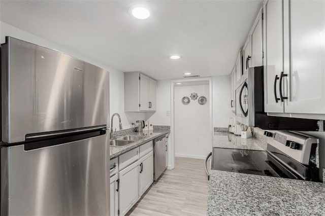 kitchen with a sink, light stone counters, white cabinetry, stainless steel appliances, and light wood-style floors