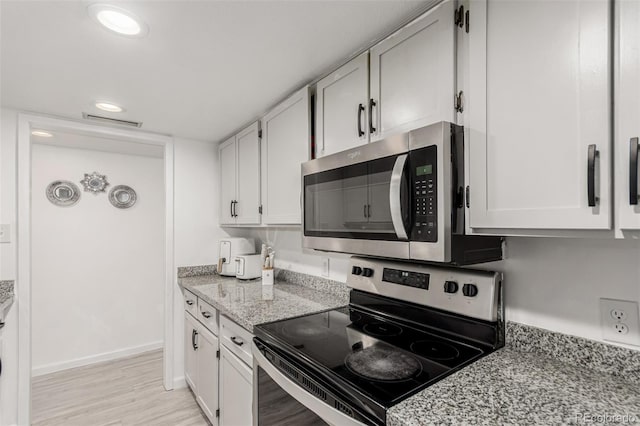 kitchen featuring visible vents, light stone counters, white cabinetry, appliances with stainless steel finishes, and light wood finished floors