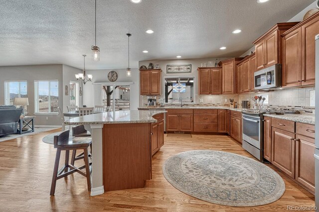 6132 Cubbage Dr, Colorado Springs, CO 80924 - kitchen with light wood-type flooring, a center island, a chandelier, appliances with stainless steel finishes, and brown cabinetry