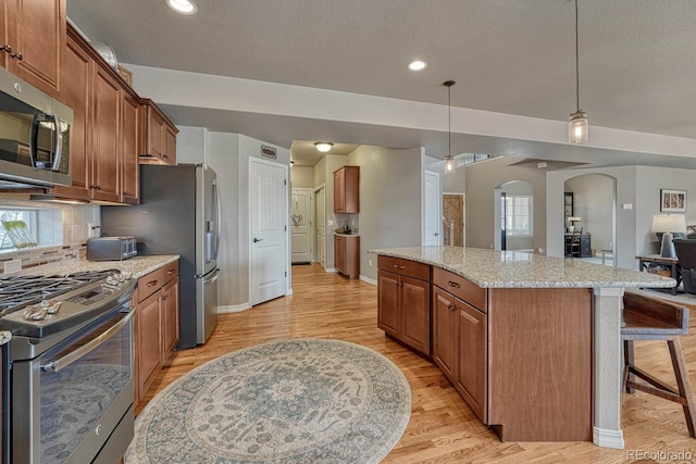6132 Cubbage Dr, Colorado Springs, CO 80924 - kitchen featuring arched walkways, tasteful backsplash, light wood-type flooring, and appliances with stainless steel finishes