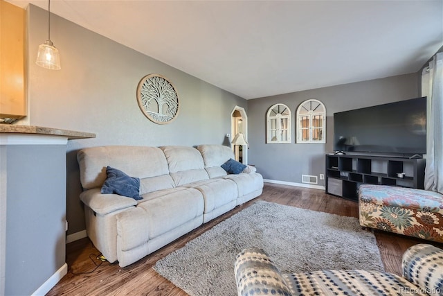 living area featuring visible vents, baseboards, arched walkways, and wood finished floors