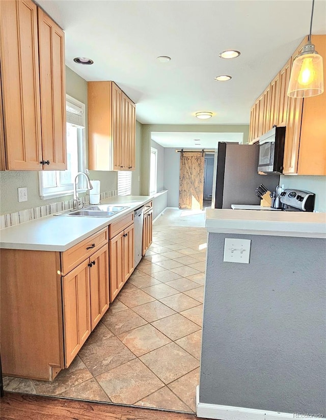 kitchen with a sink, a barn door, appliances with stainless steel finishes, light tile patterned flooring, and light countertops