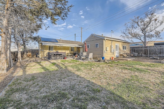 back of property with a fenced backyard, roof mounted solar panels, a jacuzzi, and a patio