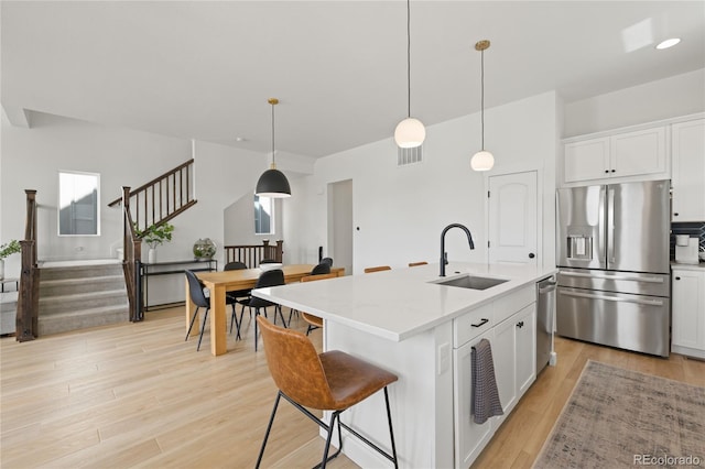 16722 Shoshone St, Broomfield, CO 80023 - kitchen with appliances with stainless steel finishes, a sink, light wood-style flooring, white cabinetry, and a kitchen island with sink