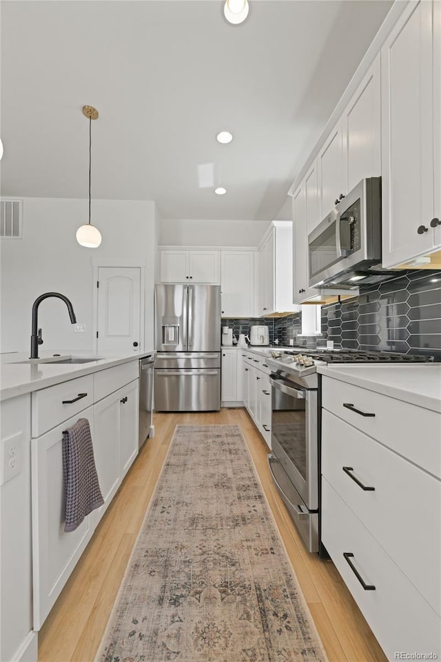 16722 Shoshone St, Broomfield, CO 80023 - kitchen with appliances with stainless steel finishes, a sink, white cabinets, backsplash, and decorative light fixtures