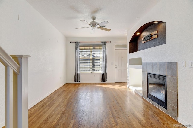 unfurnished living room featuring a tiled fireplace, ceiling fan, a textured ceiling, and light hardwood / wood-style floors