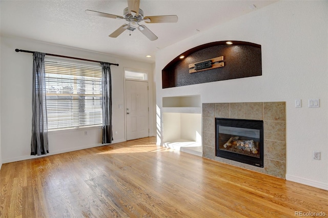 unfurnished living room with ceiling fan, a tiled fireplace, and hardwood / wood-style floors